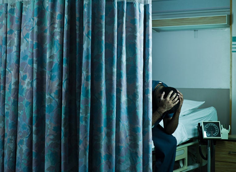 Young male doctor sitting on hospital bed with head in hands