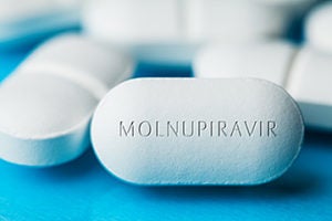 COVID-19 experimental antiviral drug MOLNUPIRAVIR,two white pills with letters engraved on side,potential experimental Coronavirus cure for pandemic outbreak crisis,isolated on blue background