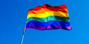 Rainbow flag waving in the wind against clear blue sky