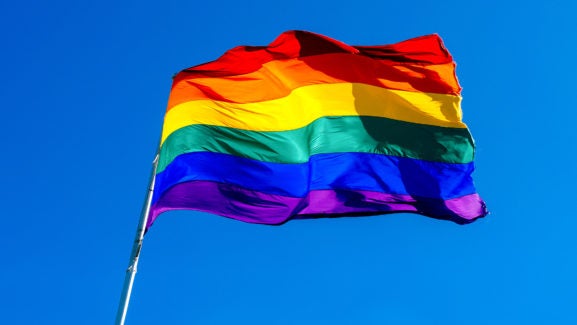 Rainbow flag waving in the wind against clear blue sky