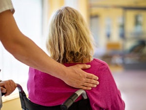 Rear view shot of a senior female sitting in wheelchair pushed by a healthcare worker are in hospital. Nurse helping a patient in wheelchair.