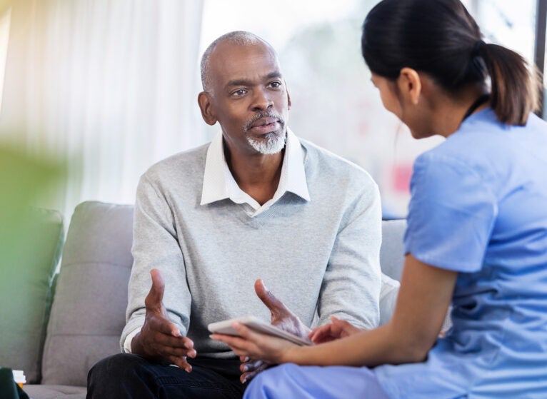 Senior African American man gestures while asking a female healthcare professional a question about his diagnosis.