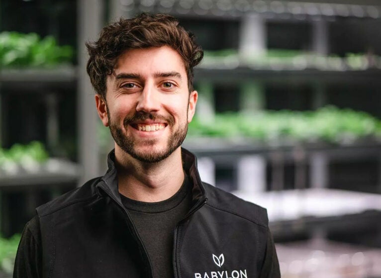 Co-founder of Babylon Micro-Farms and biomedical engineering alumnus Graham Smith stands in front of the mini produce gardens he helped develop. (Contributed photo)