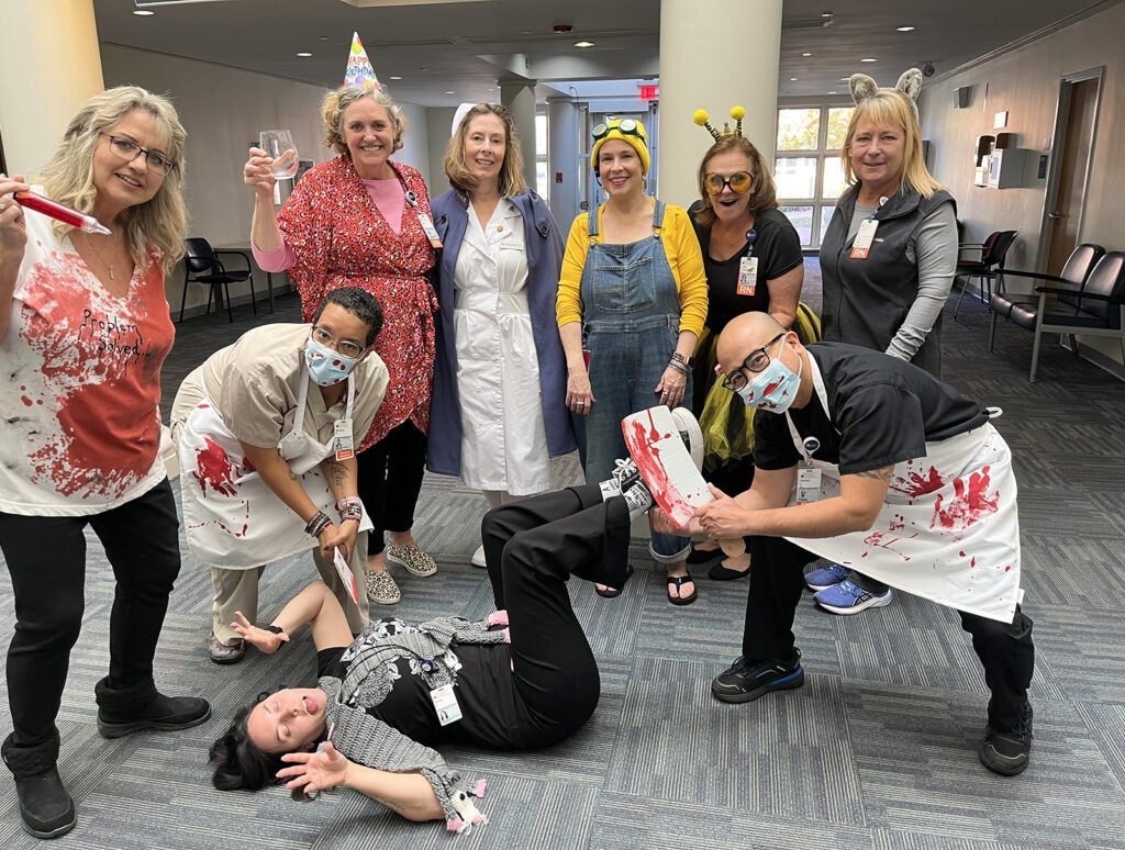 Happy Halloween from Employee Health | “No one plays Opossum at Employee Health”: (l-r ) Jackie Brady, CMA (Problem Solver); Monique Page, CMA (Butcher Queen); Anne Schueneman, RN (Party Animal); Margaret Zayas, FNP (Nurse Ratchet); Prim Winter (Minion); Tricia Cady, RN (Bumble Bee); Colleen Di Cesare, RN (Bid Bad Gray Wolf); Antonio Lambio, RN (Butcher King); and Kelsey Pleasants (Opossum, not sleeping).