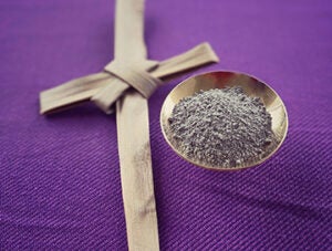 Holy ash and a cross made of palm leaf arranged on purple background.