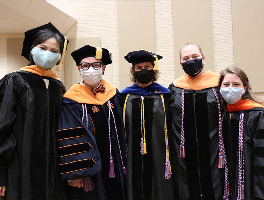 Yost (center) poses with DNP graduates in 2021, including now-professor Ashley Apple (second from left), wearing a blue velvet gift hood from her student advisees . . .