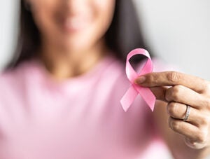 Detail of a female hand holding pink ribbon towards the camera to raise breast cancer awareness.