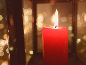 A close view of a red pillar candle burning brightly inside a lantern, its flame reflected across the glass panels. Warm golden tones and soft bokeh create a serene, calm and atmospheric holiday moment, perfect for Christmas and New Year themes. Copy space for text, high angle view - Christmas, concepts & ideas