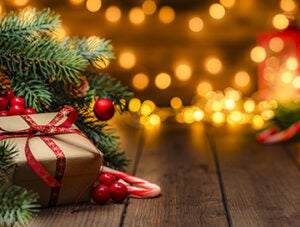 Christmas present wrapped with craft paper and red ribbon under the Christmas tree in a cozy festive atmosphere with defocused Christmas lights at background
