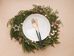 Golden and black knife and fork in white plate. Christmas wreath decoration. Festive table setting for Christmas.