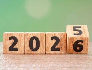 3D render of wooden cubes flipping from 2025 to 2026 on a tabletop with soft green bokeh background. No people. New Year changeover concept, copy space.