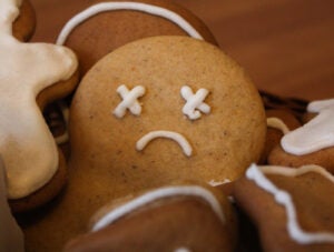 Homemade gingerbread men in the woven basket on the wooden table. Depressed christmas cookie with sad face covered with icing. New Year pastry in the shape of stars and men. Winter background