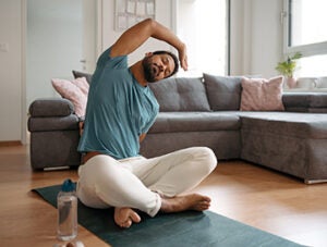 The single man exercising alone at home, stretching his back and arm. Young man is happy, relaxed, and content with his life. Solo home workout and meditation, morning or evening workout routine.