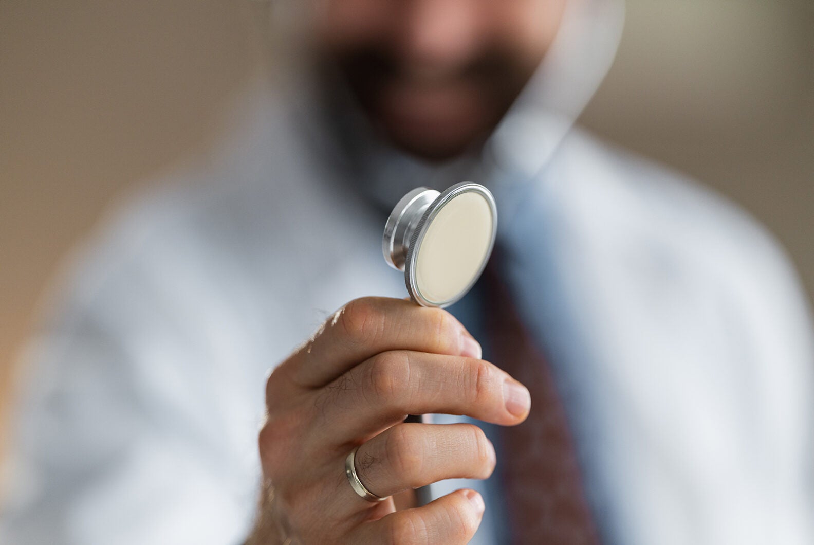 Doctor holds a stethoscope toward the camera in a close-up shot, suggesting medical examination, professional care and trust during a clinical consultation with shallow depth of field and warm tones.