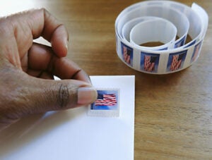 Close-up of unrecognizable black woman placing postage stamp on envelope