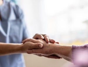 A close-up of a nurse in a blue uniform holding the hand of an elderly person with compassion. This moment exudes a strong sense of support, humanity, and care in a healthcare setting or retirement home.