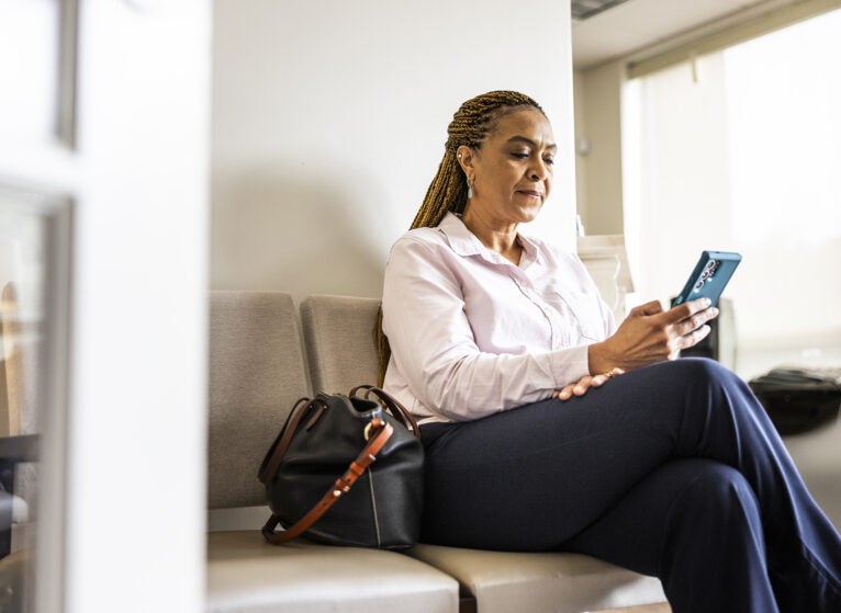 Mid adult woman using smartphone in doctor's office waiting room