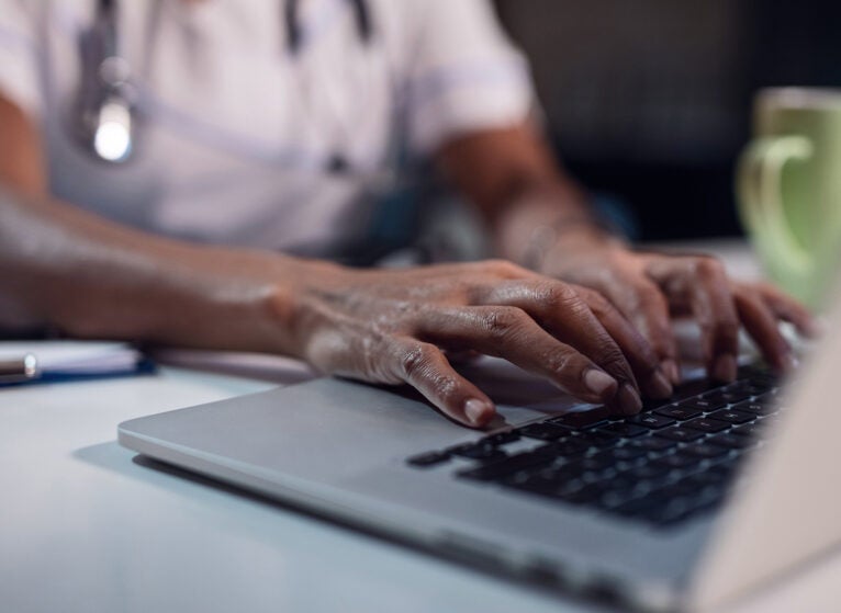 Close up of Black doctor typing on computer while working at office desk.