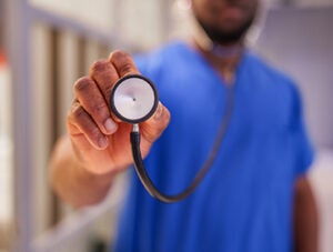A close-up shot of a healthcare worker’s hand holding a stethoscope, emphasizing the essential tools used in patient care.
